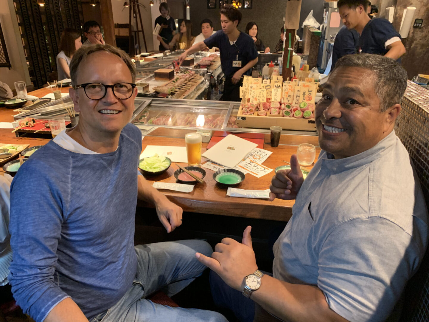 Two men sitting at a table in front of sushi.