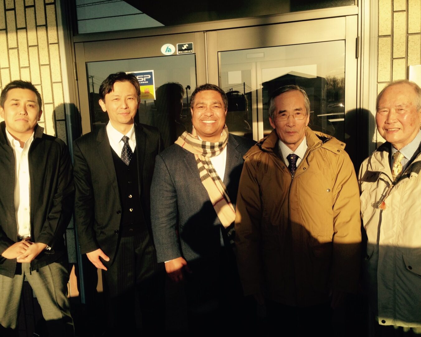 Five men in coats smiling outside a doorway