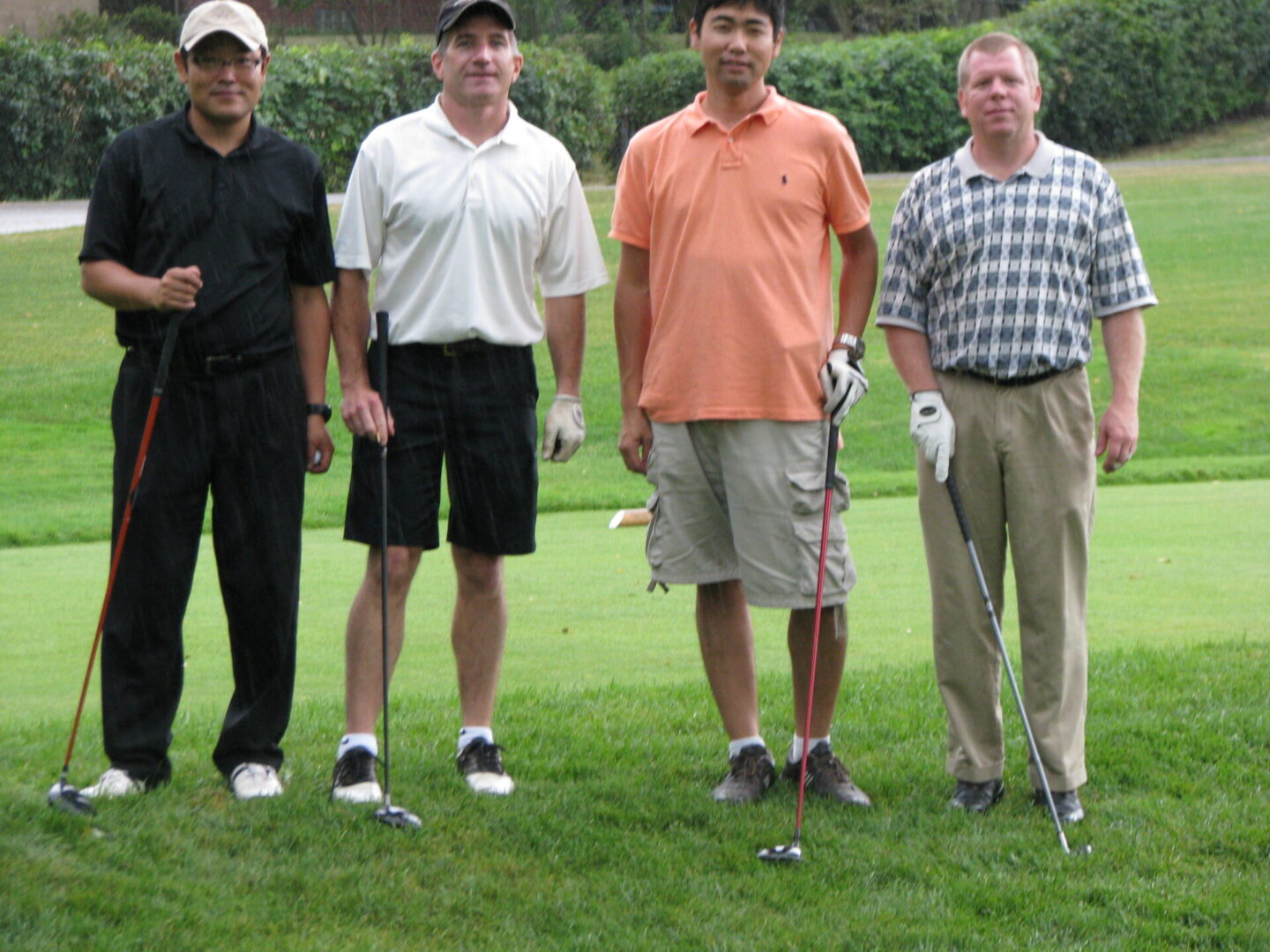 Four men standing on a golf course holding onto their clubs.