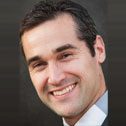 Smiling man wearing gray suit, dark backdrop